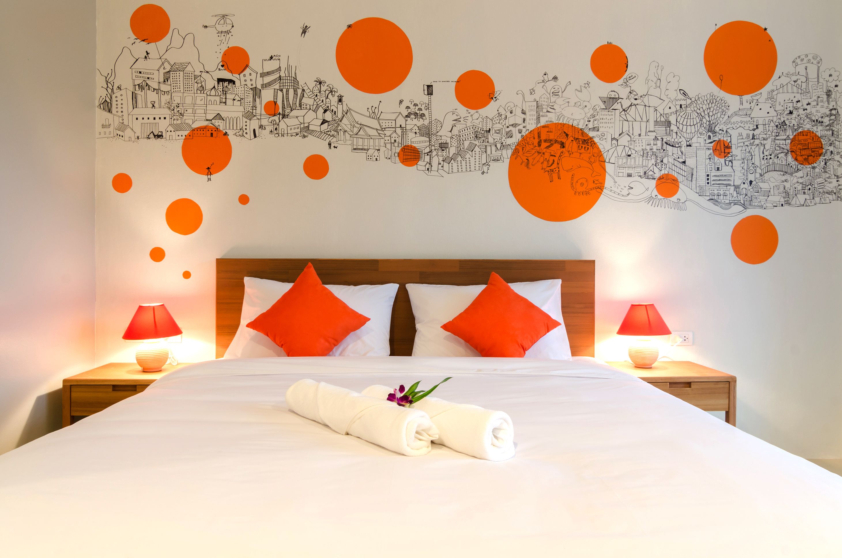 Une chambre d’hôtel avec un grand lit, deux tables de chevet, des lampes rouges et une fresque murale.