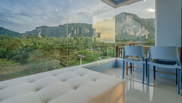 A modern room with a large glass wall offering a scenic mountain view. There is a plush sofa and two blue chairs. - Aonang Miti Resort (Krabi)