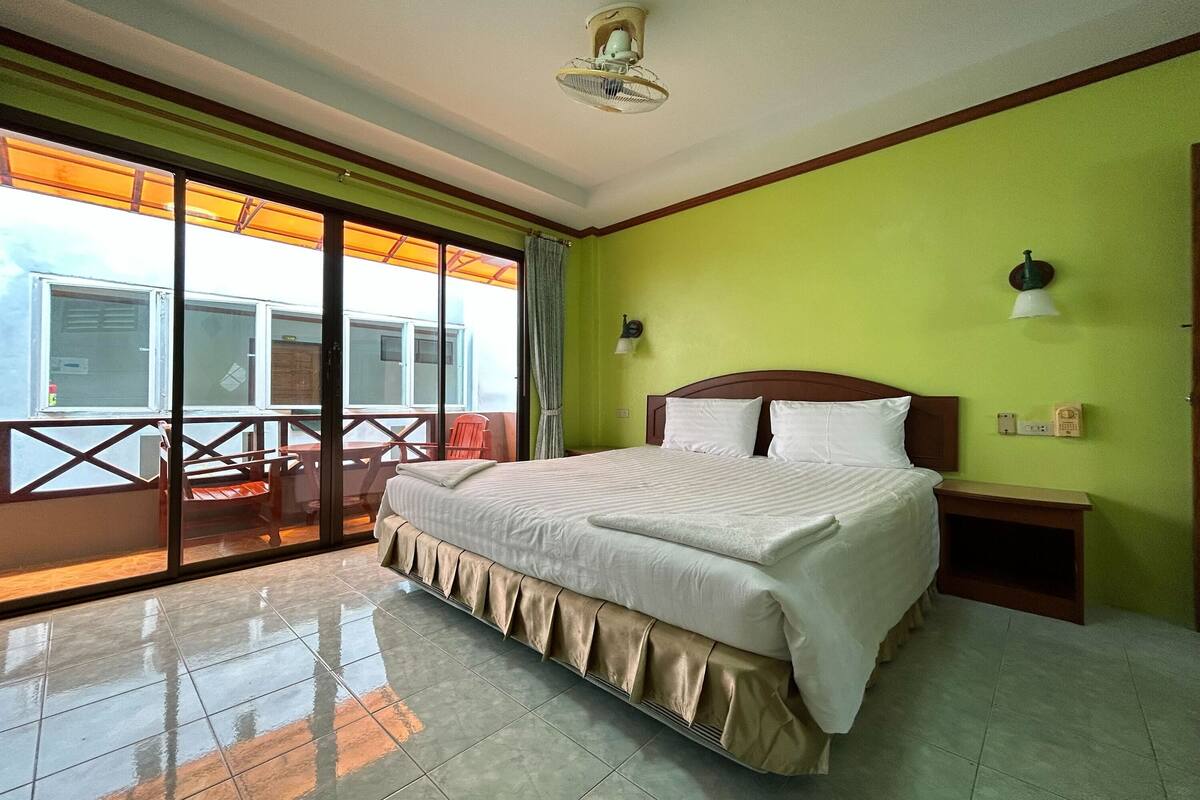 A hotel room with a bed, a nightstand, a wall-mounted lamp, and a sliding glass door leading to an outdoor area with a table and chairs.