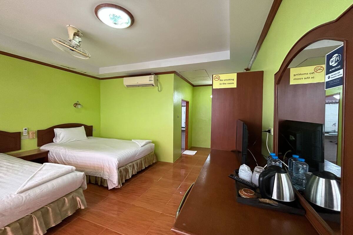 A hotel room with two beds, a TV, a mirror, and a kitchenette area.