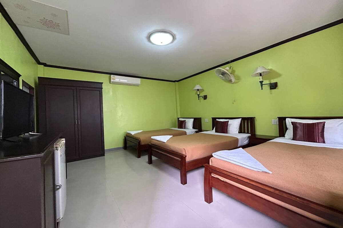 A hotel room with two single beds, a desk with a computer, a wardrobe, and a ceiling fan.
