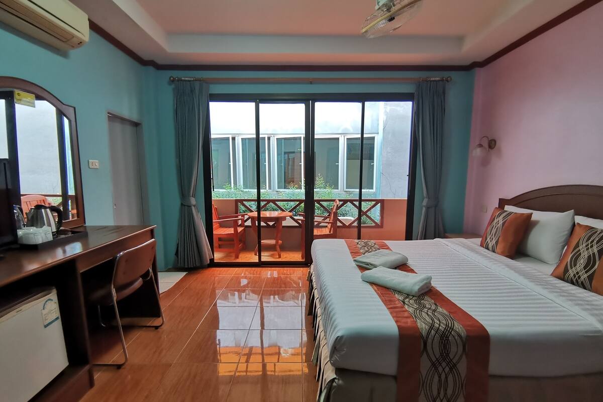 A hotel room with a bed, desk, and a balcony with a table and chairs.