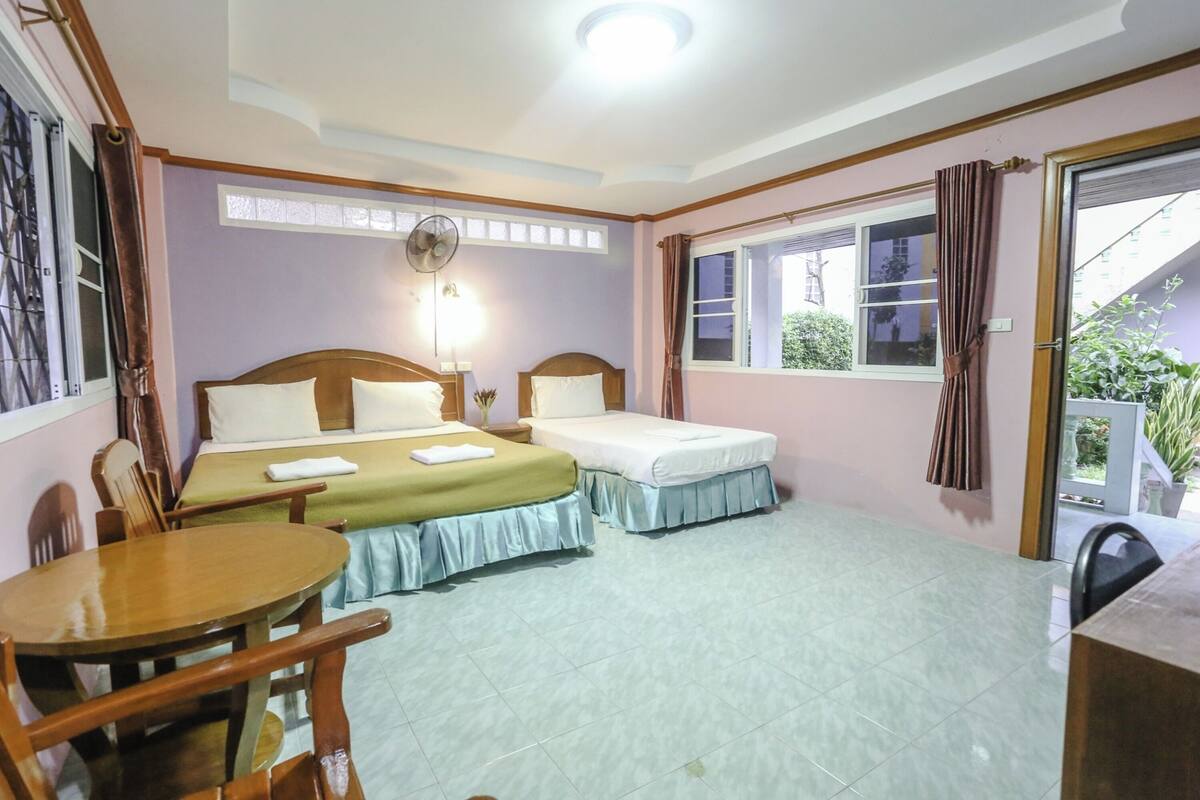 A room with two beds, a table, chairs, a fan, and a window with curtains.