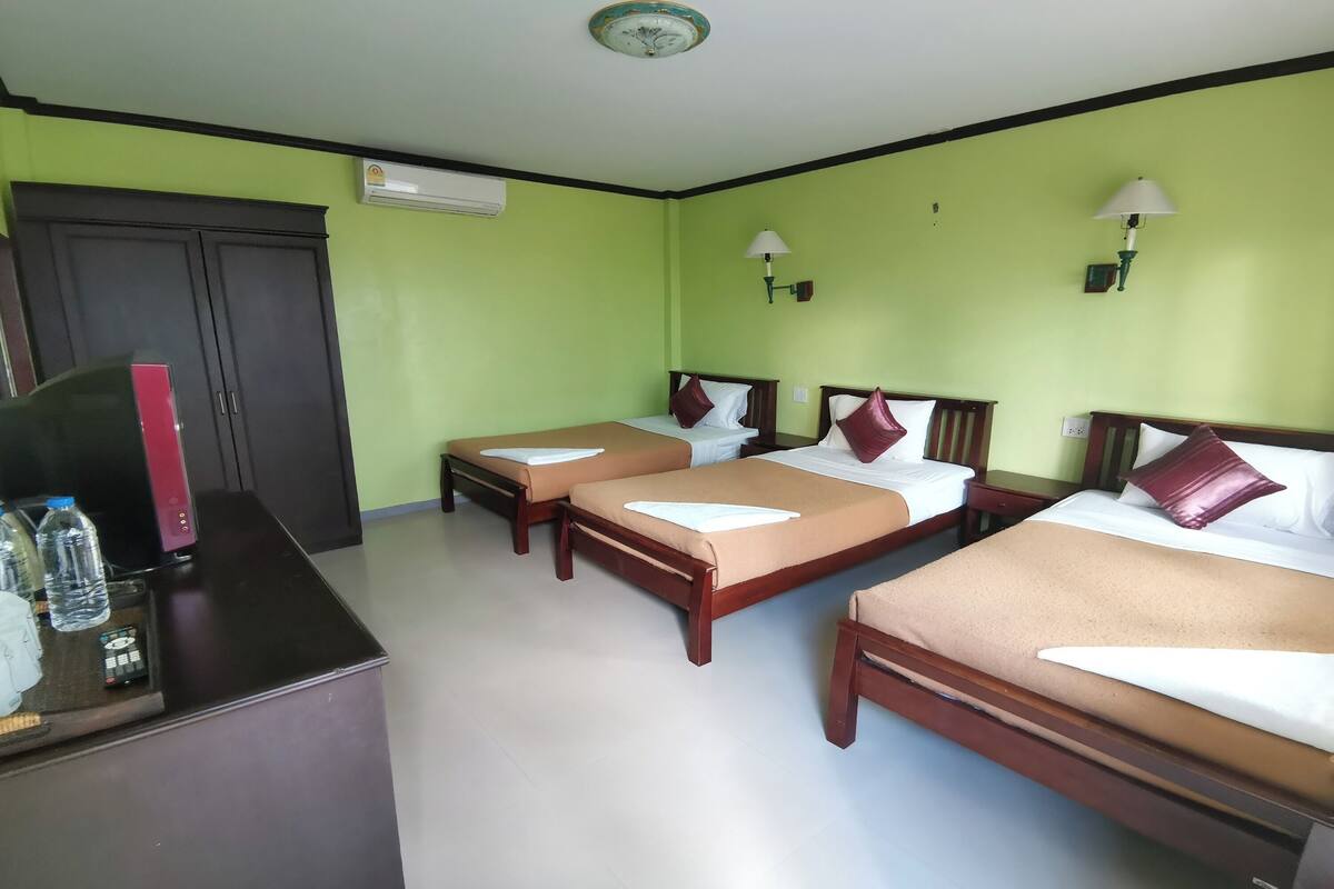 A hotel room with three beds, a desk with a telephone, and a wardrobe.