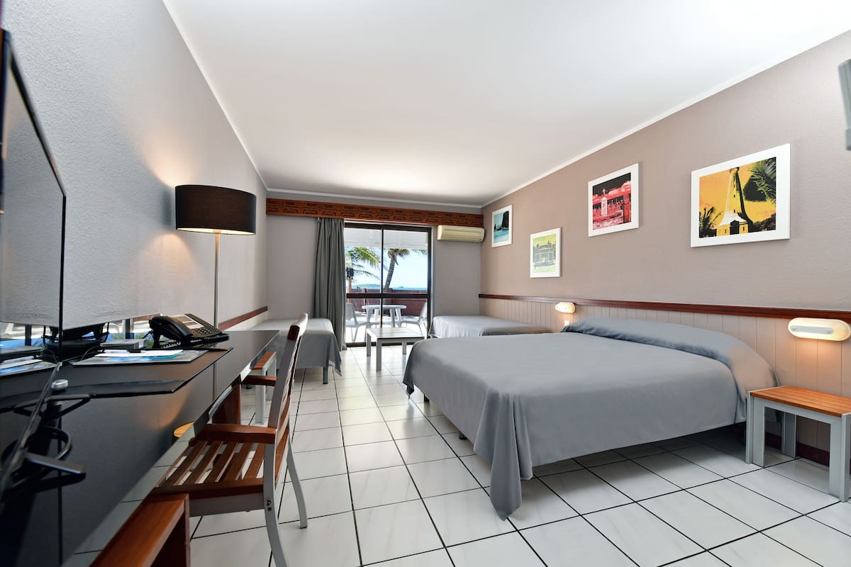 Une chambre d’hôtel équipée d’un bureau, de deux lits, d’une petite table, d’un banc et d’un balcon avec vue.