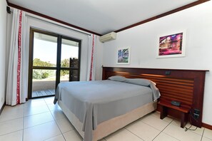 A bedroom with a bed, a nightstand, a wall-mounted air conditioner, and a door leading to an outdoor area. - Le Stanley Hotel and Suites (Nouméa)