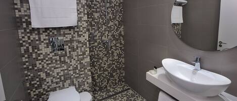 Un baño con ducha azulejada, inodoro, lavabo y espejo.