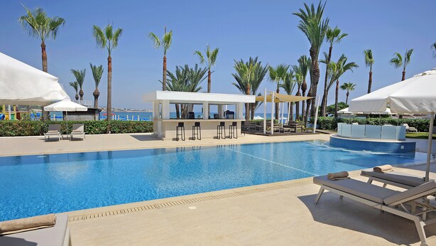 Zona de piscina con sillones de descanso, sombrillas y un bar.