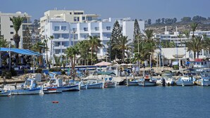 Un puerto deportivo con varias embarcaciones amarradas, rodeado de edificios y palmeras.