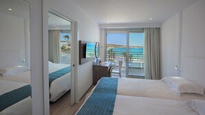 Habitación de hotel con dos camas, un escritorio, una silla, un televisor y un balcón con vistas al mar.