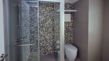 Un baño moderno con ducha separada por mampara de vidrio, paredes revestidas de azulejos y un inodoro.
