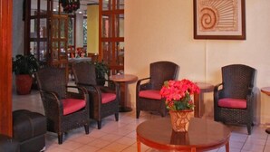 Un hall con sillas de mimbre, una mesa de centro de vidrio y una planta con flores rojas.
