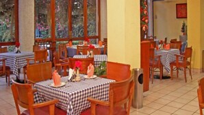 Un restaurante con manteles a cuadros, sillas de madera y grandes ventanales con vistas a zonas verdes.