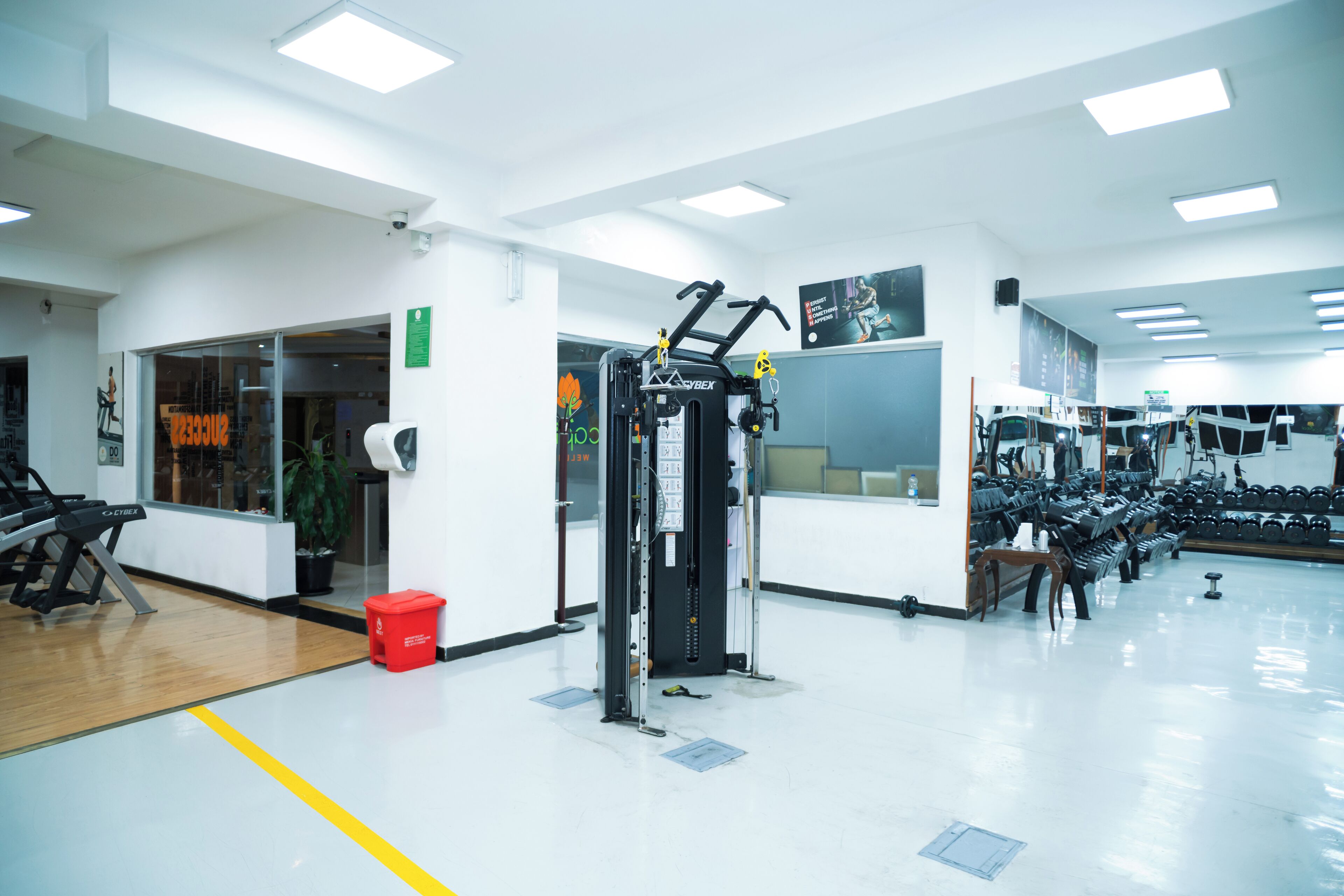 Un gimnasio con equipo de ejercicio, una cinta de correr y un bote de basura rojo.