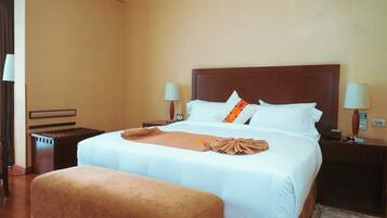 Una habitación de hotel con una cama grande, dos mesitas de noche, un banco y dos lámparas.
