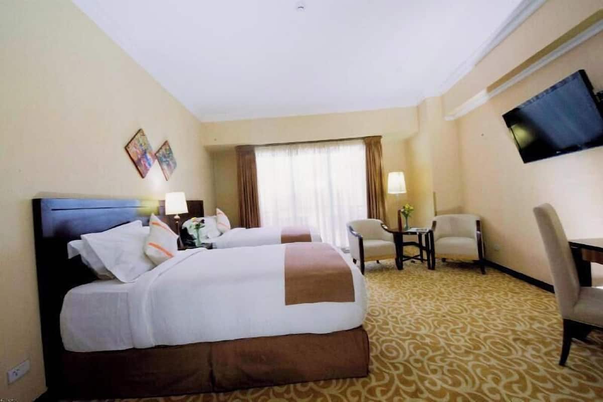 A hotel room with two beds, a TV, a desk, and a chair.