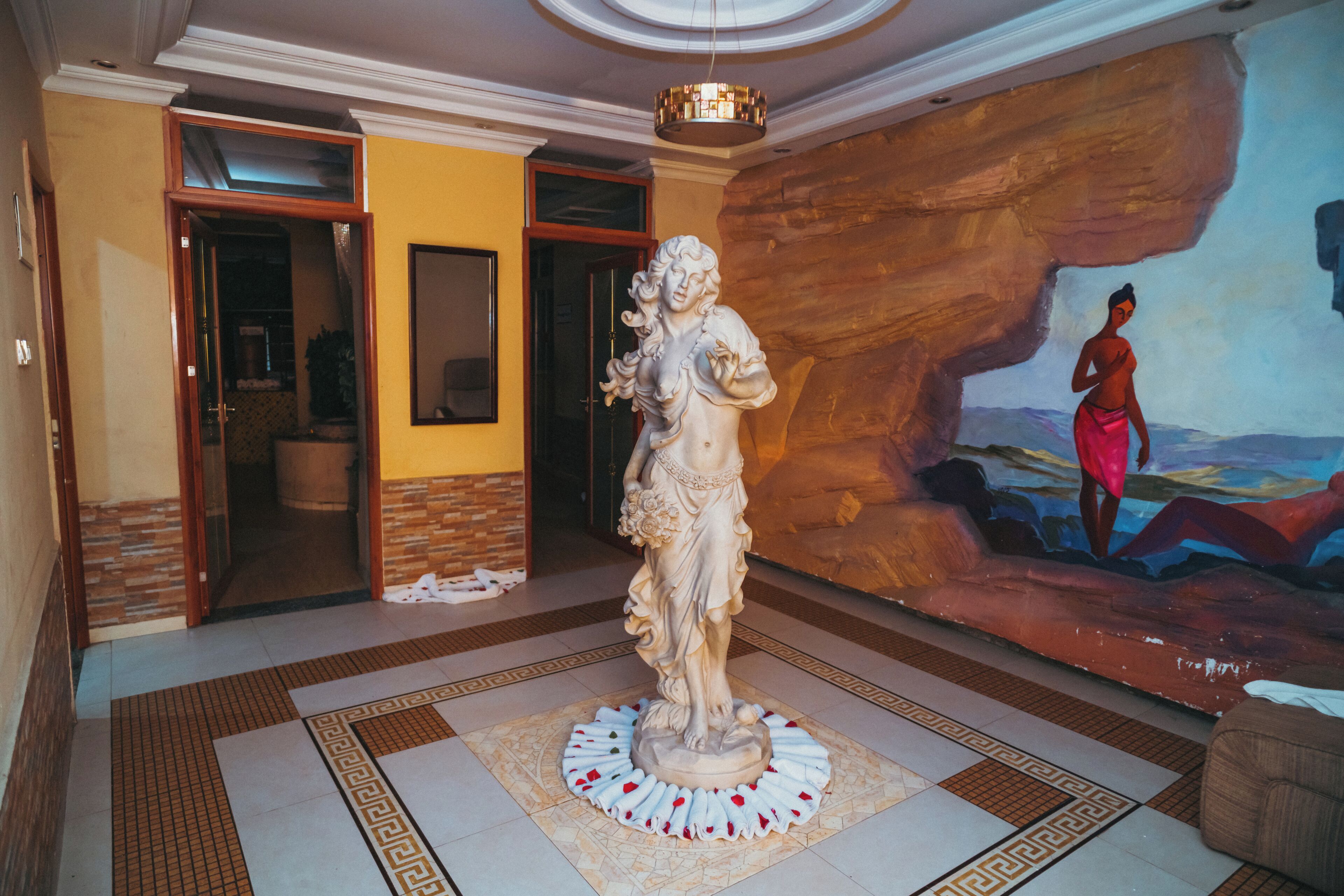 A statue in a lobby with a mural on the wall.