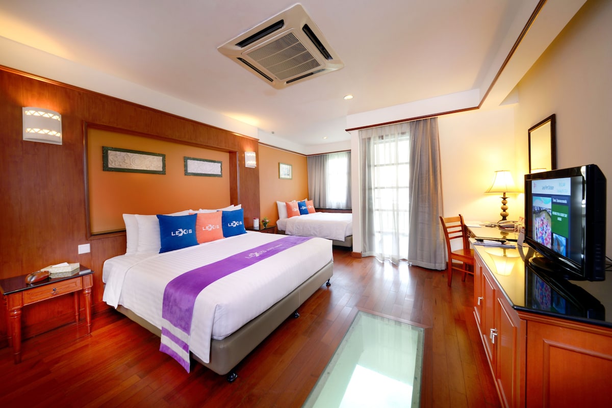 A hotel room with two beds, a desk with a computer, a TV, and a window with curtains.