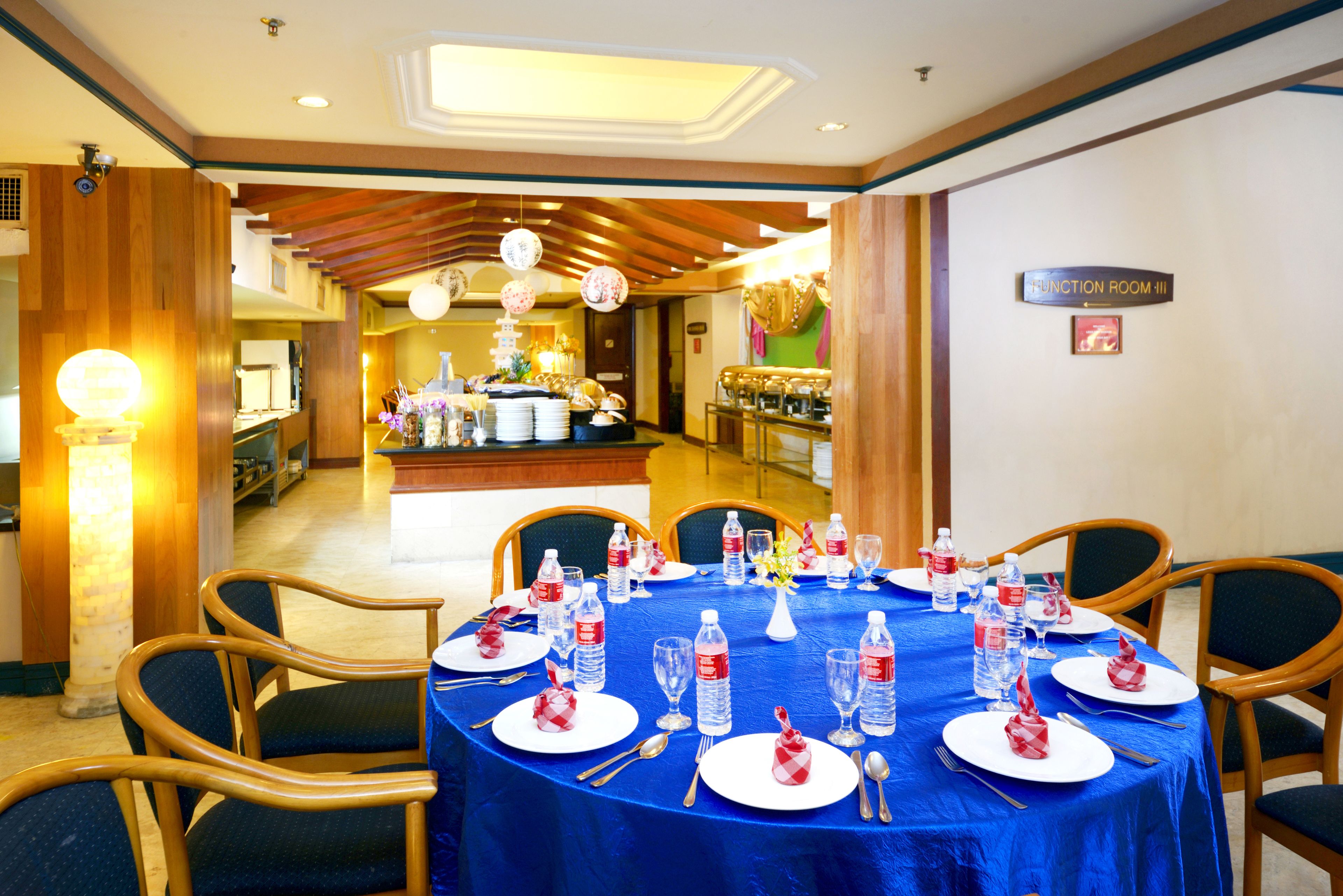 Un espace repas avec des tables rondes mises pour le service, agrémenté de bouteilles d’eau, de verres et de couverts.