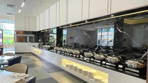 Una cocina moderna con una isla central que exhibe recipientes de comida, un área de comedor con sillas y mesas, y vistas al exterior a través de grandes ventanales.