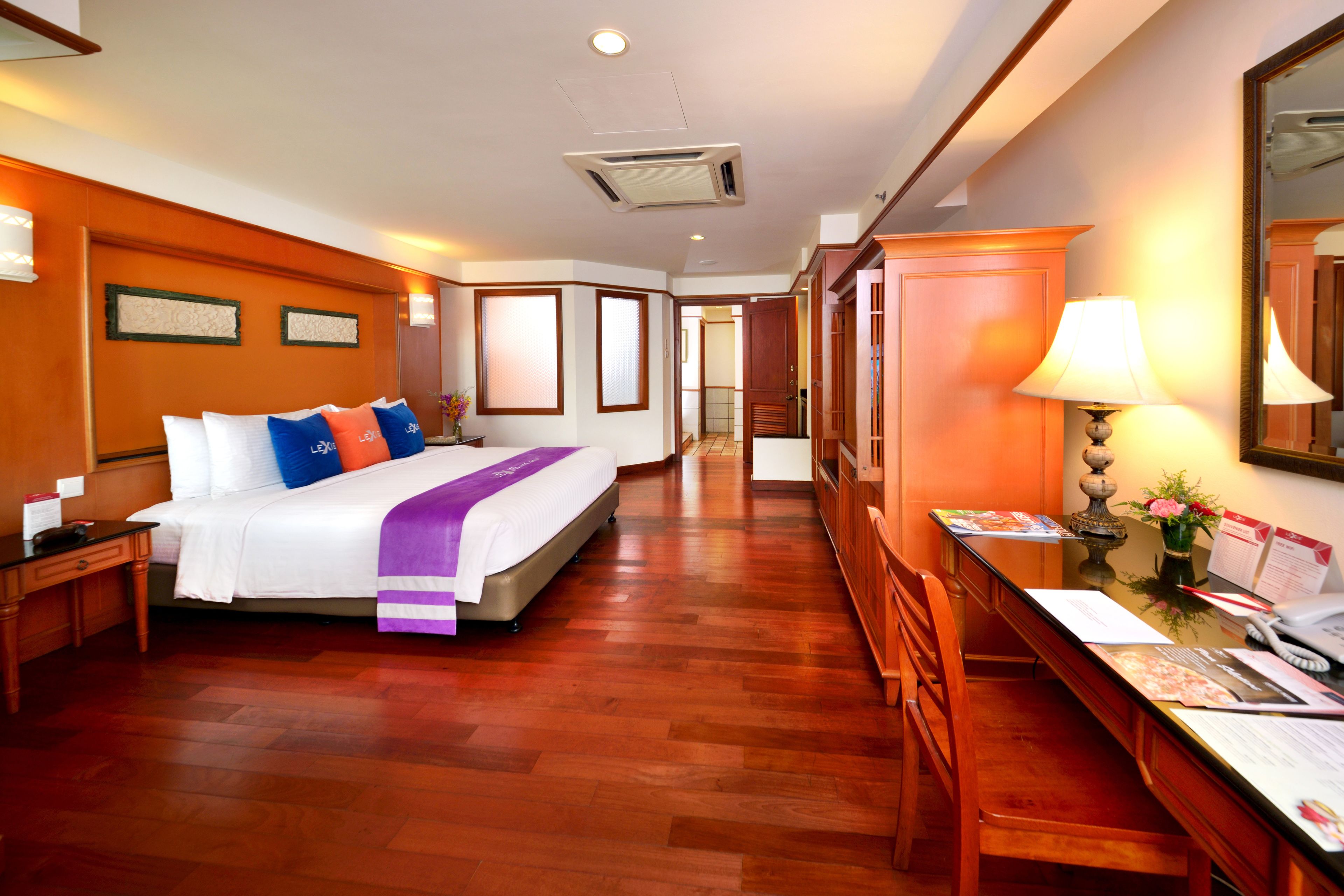 Habitación de hotel con una cama grande, suelo de madera, un escritorio con lámpara y un espejo en la pared.