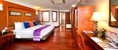 Habitación de hotel con una cama grande, suelo de madera, un escritorio con lámpara y un espejo en la pared.