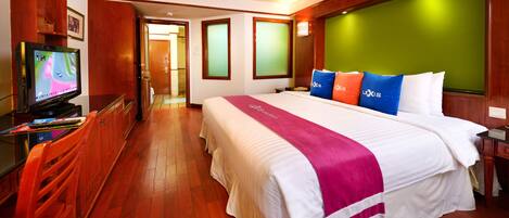 A hotel room with a large bed, wooden flooring, a television, and a desk with a chair.
