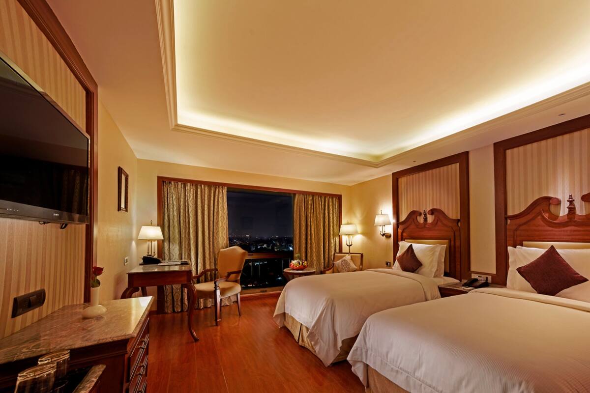 Habitación de hotel con dos camas, un escritorio, una silla y un televisor.