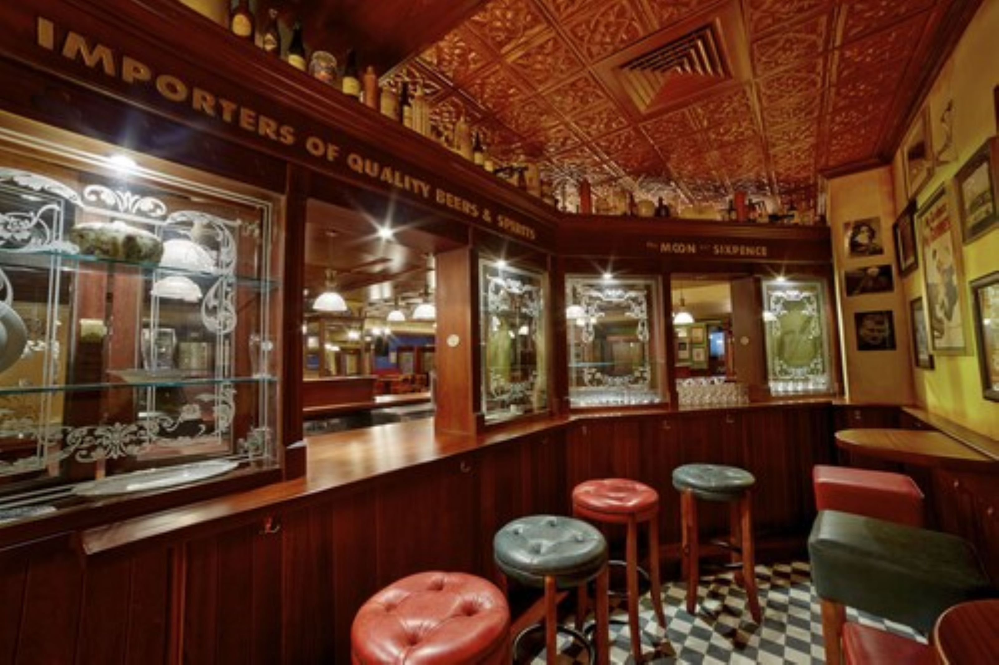 Una zona de bar con paneles de madera, taburetes y suelo a cuadros.