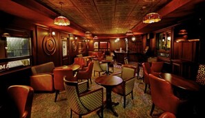 A dimly lit bar area with wooden furniture and patterned carpet. - Hablis Hotel (Chennai)