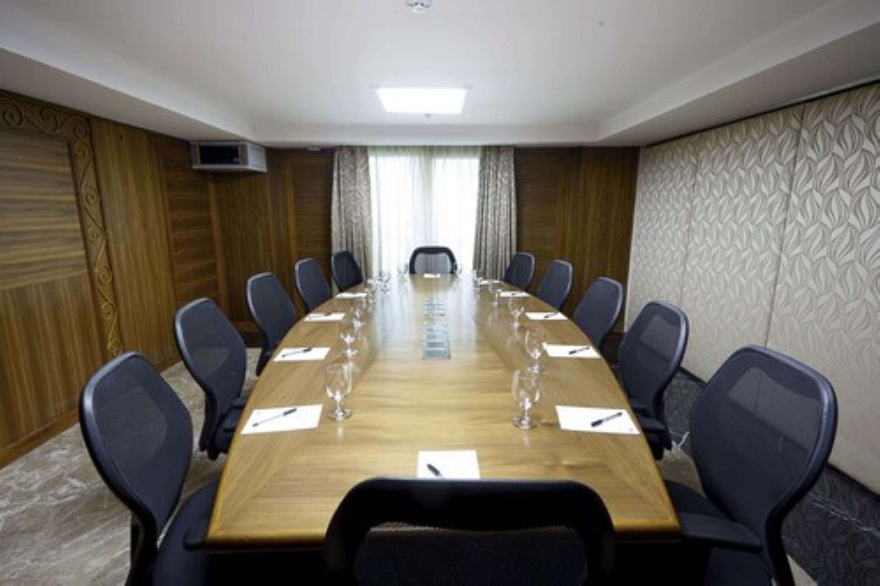 Un salón de conferencias con una larga mesa, sillas y una pantalla para proyector.