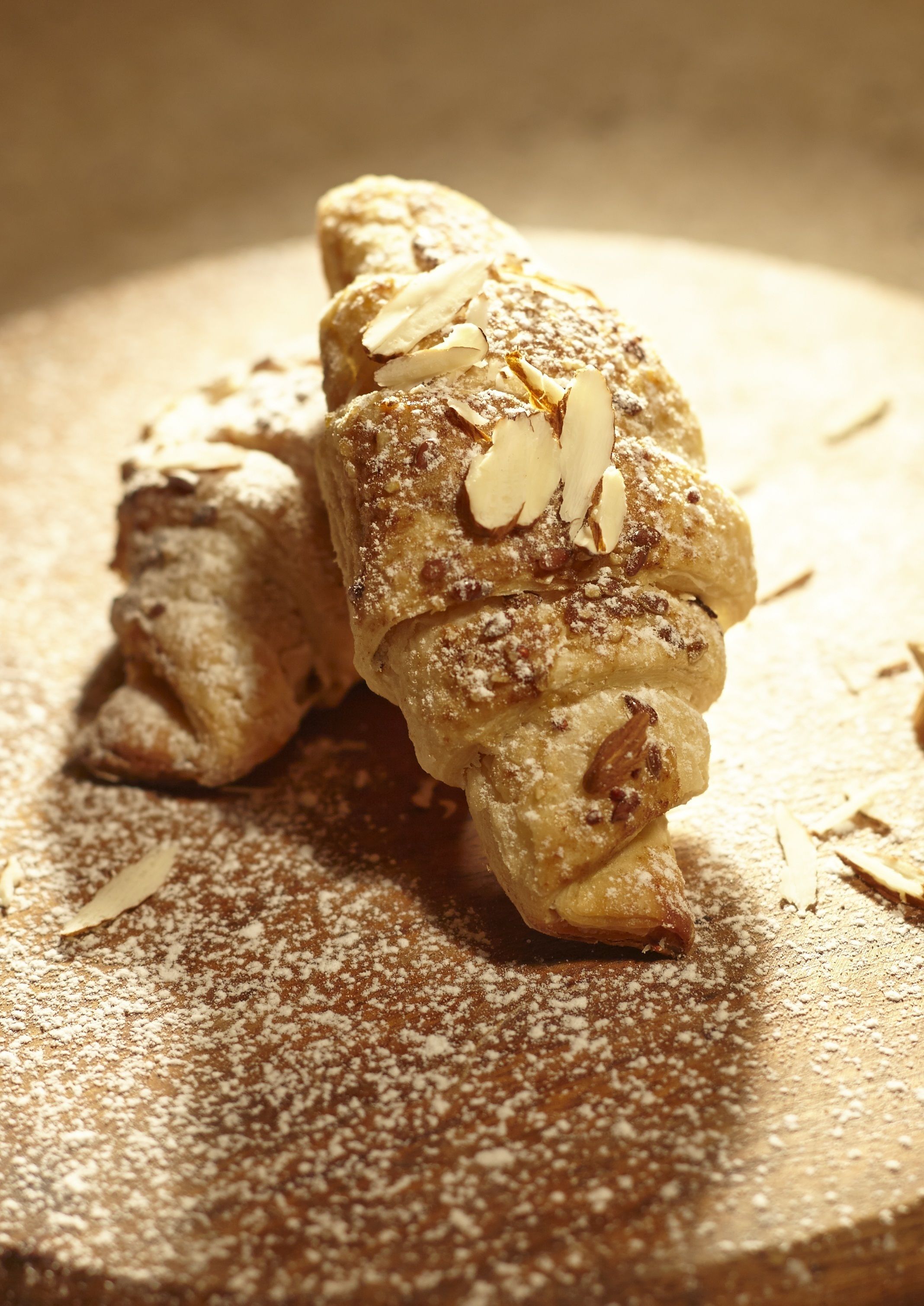 A pastry with almonds on a wooden surface.