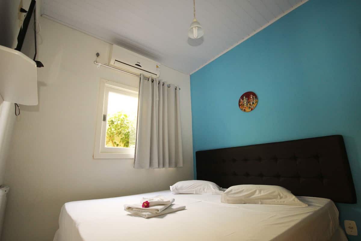 Ein Schlafzimmer mit einem Bett, einem Fenster mit Vorhängen, einer Wandklimaanlage und einer Wanddekoration.
