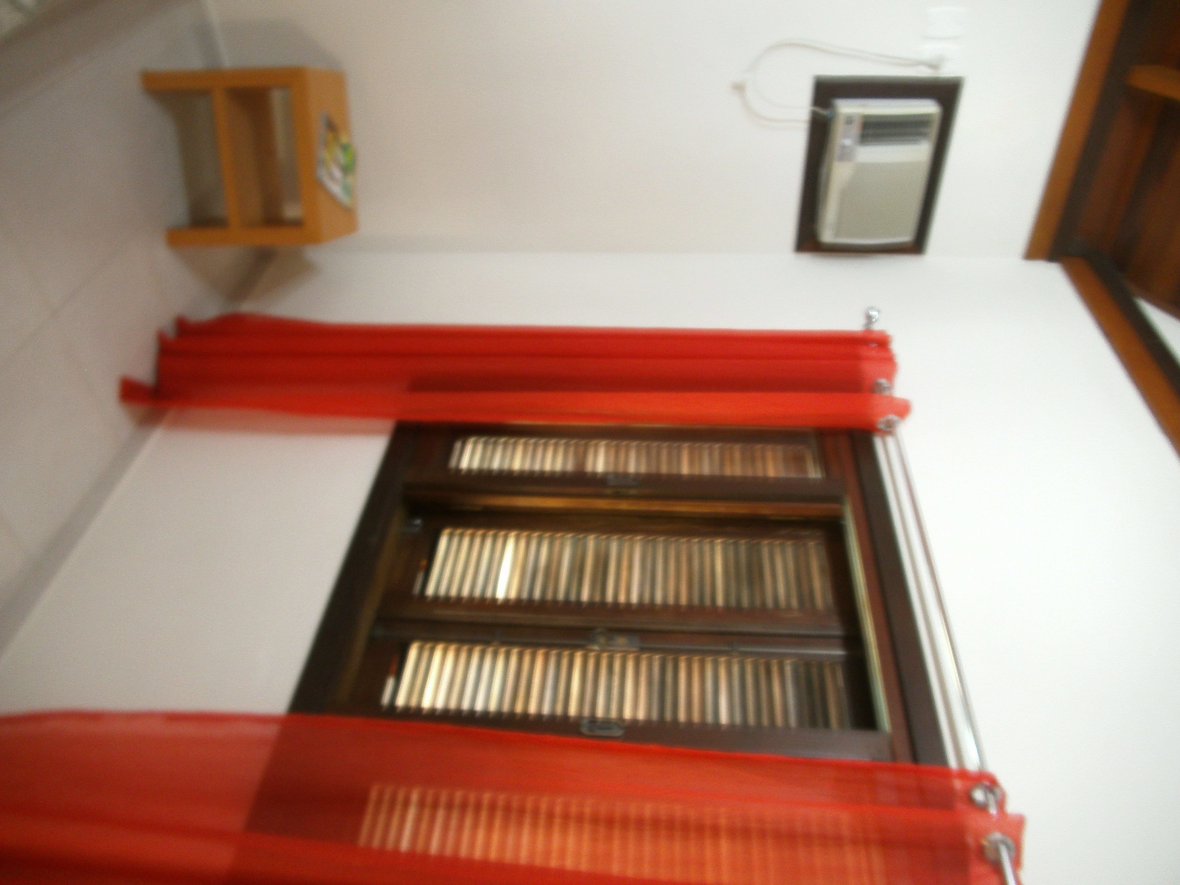 A room with a window covered by red curtains, a wooden shelf, and a wall-mounted air conditioning unit.