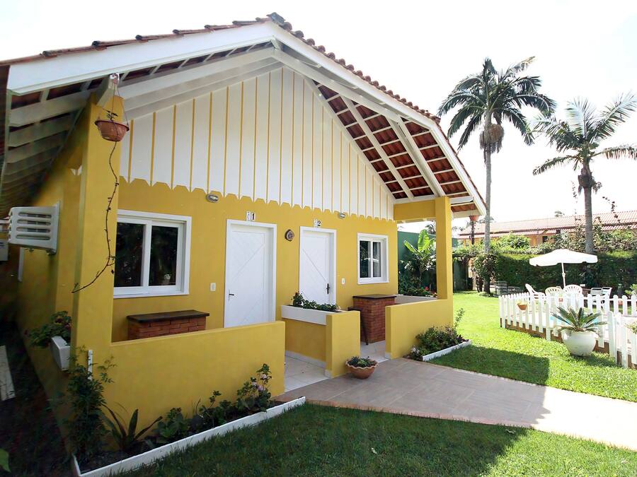 Un edificio amarillo con un porche cubierto, puertas blancas y un pequeño jardín con macetas y una cerca de piquetes blancos.