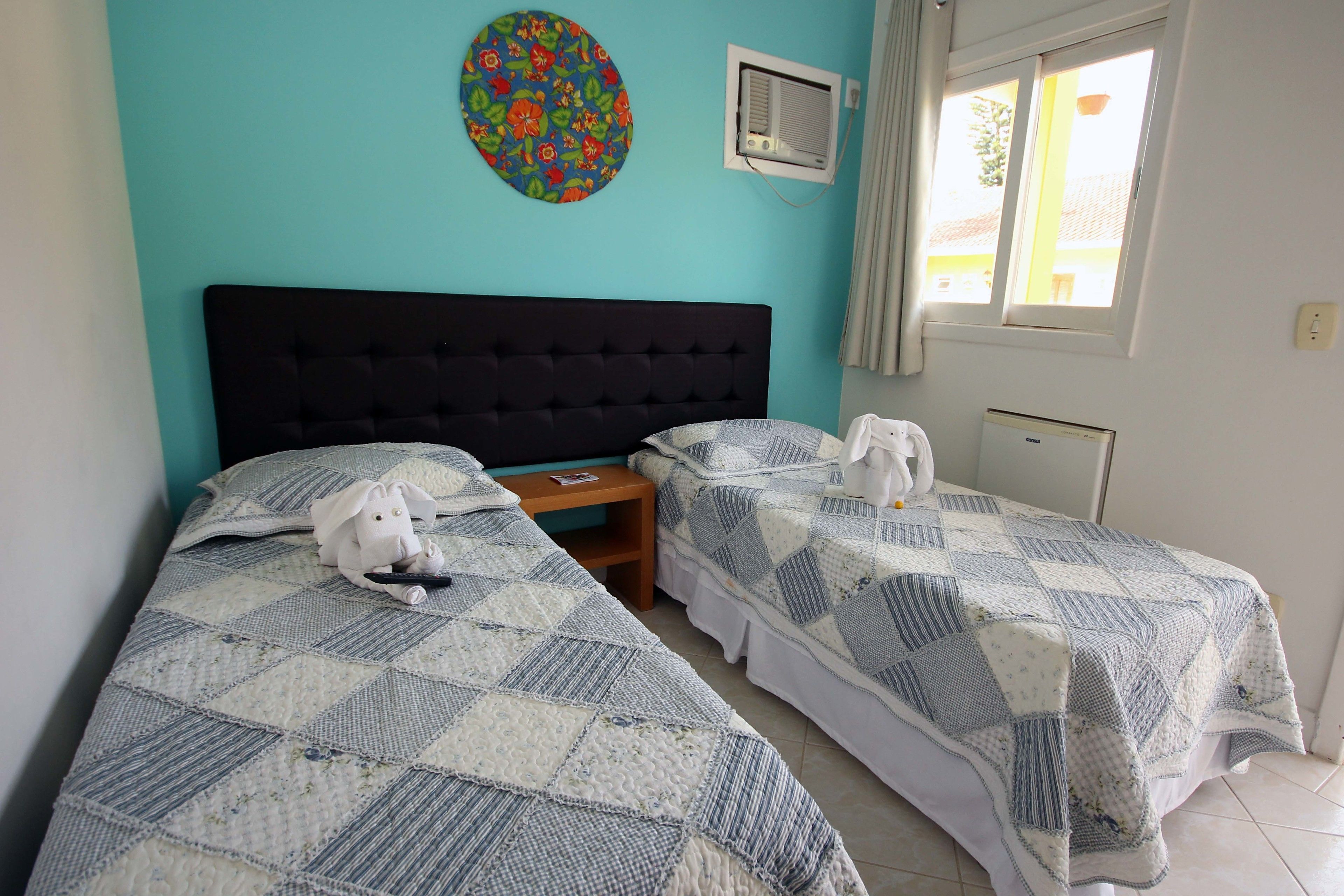 A room with two beds, a round wall decoration, an air conditioning unit, and a window with curtains.
