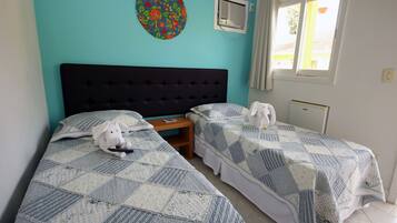 Una habitación con dos camas, un adorno circular en la pared, un equipo de aire acondicionado y una ventana con cortinas.