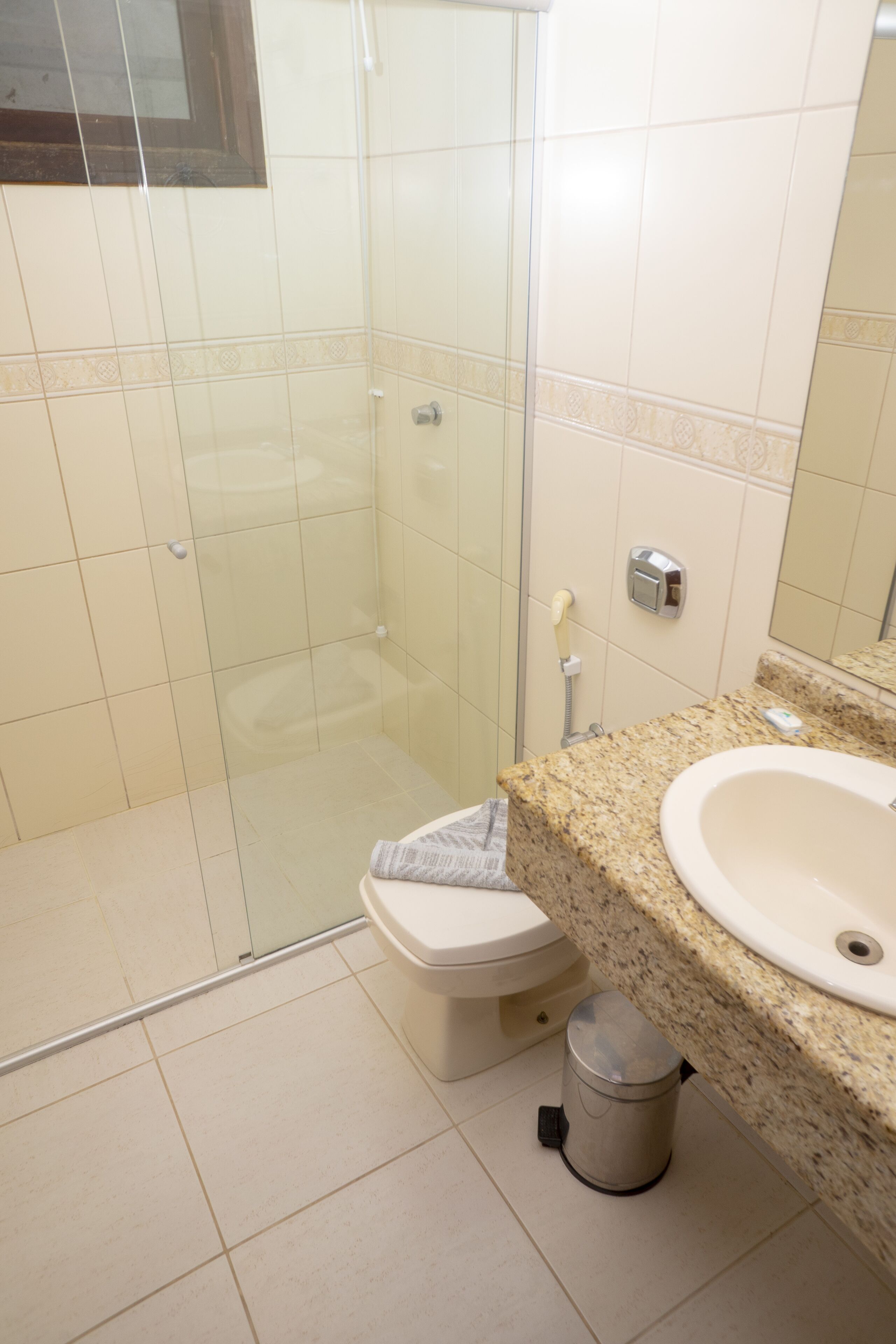 A bathroom with a glass-enclosed shower, a toilet, a sink, and a trash can.