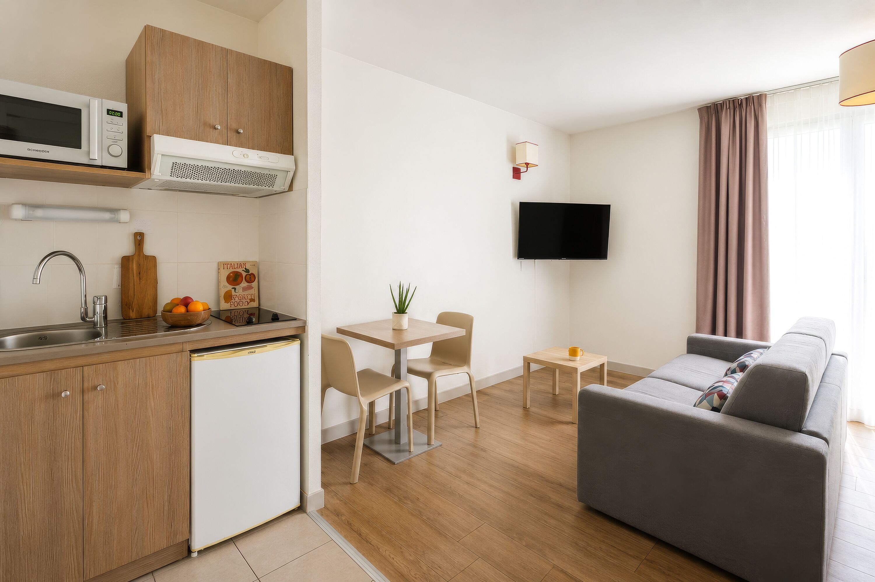 Un espacio habitable compacto con kitchenette, comedor, sofá y televisor montado en la pared.