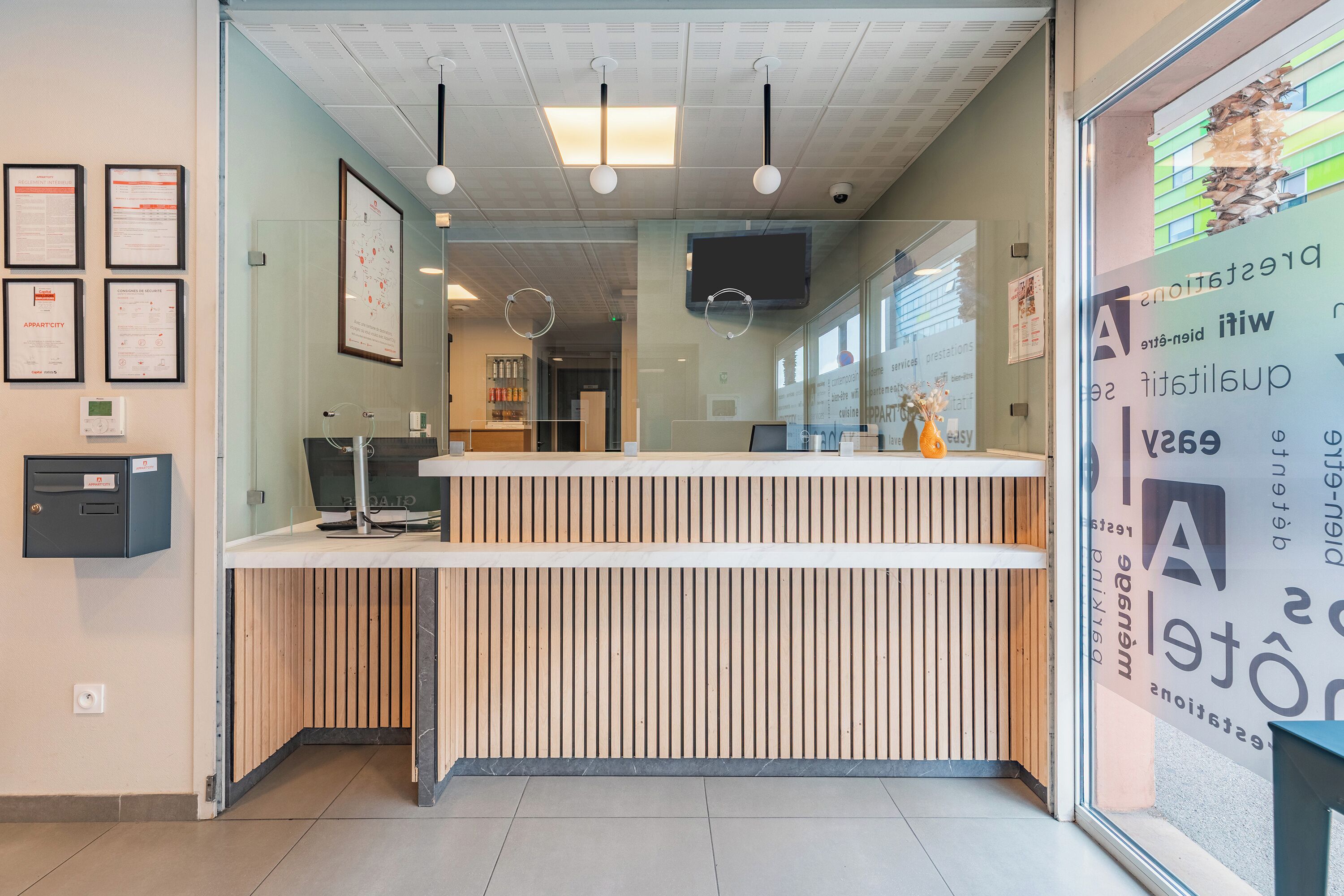 A reception desk with a modern design, framed certificates on the wall, and a digital screen above it.