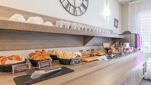 A breakfast buffet with various pastries and bread, a coffee machine, and a clock on the wall.