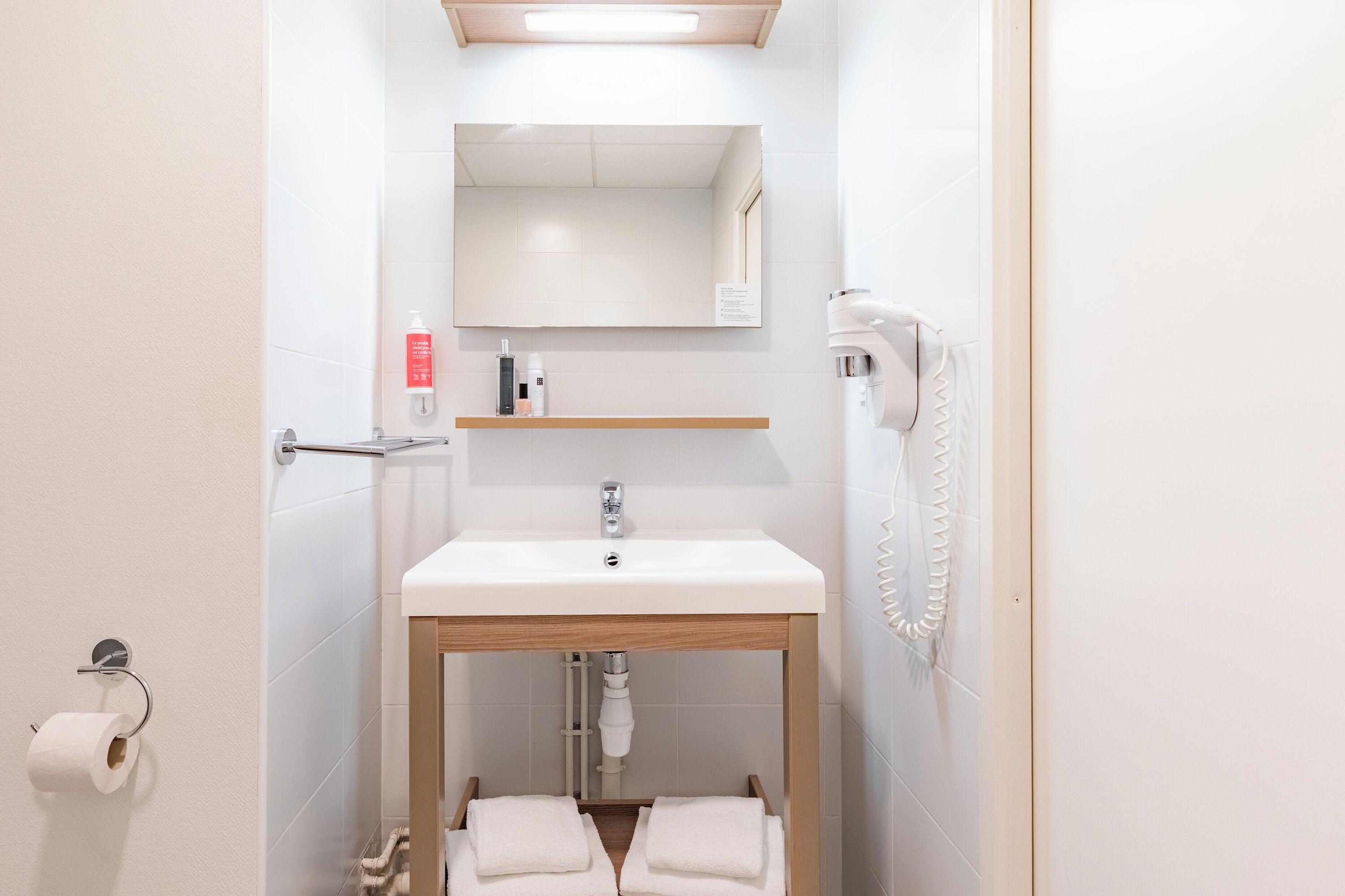 A bathroom with a white sink, a mirror, a towel rack, and a toilet paper holder.