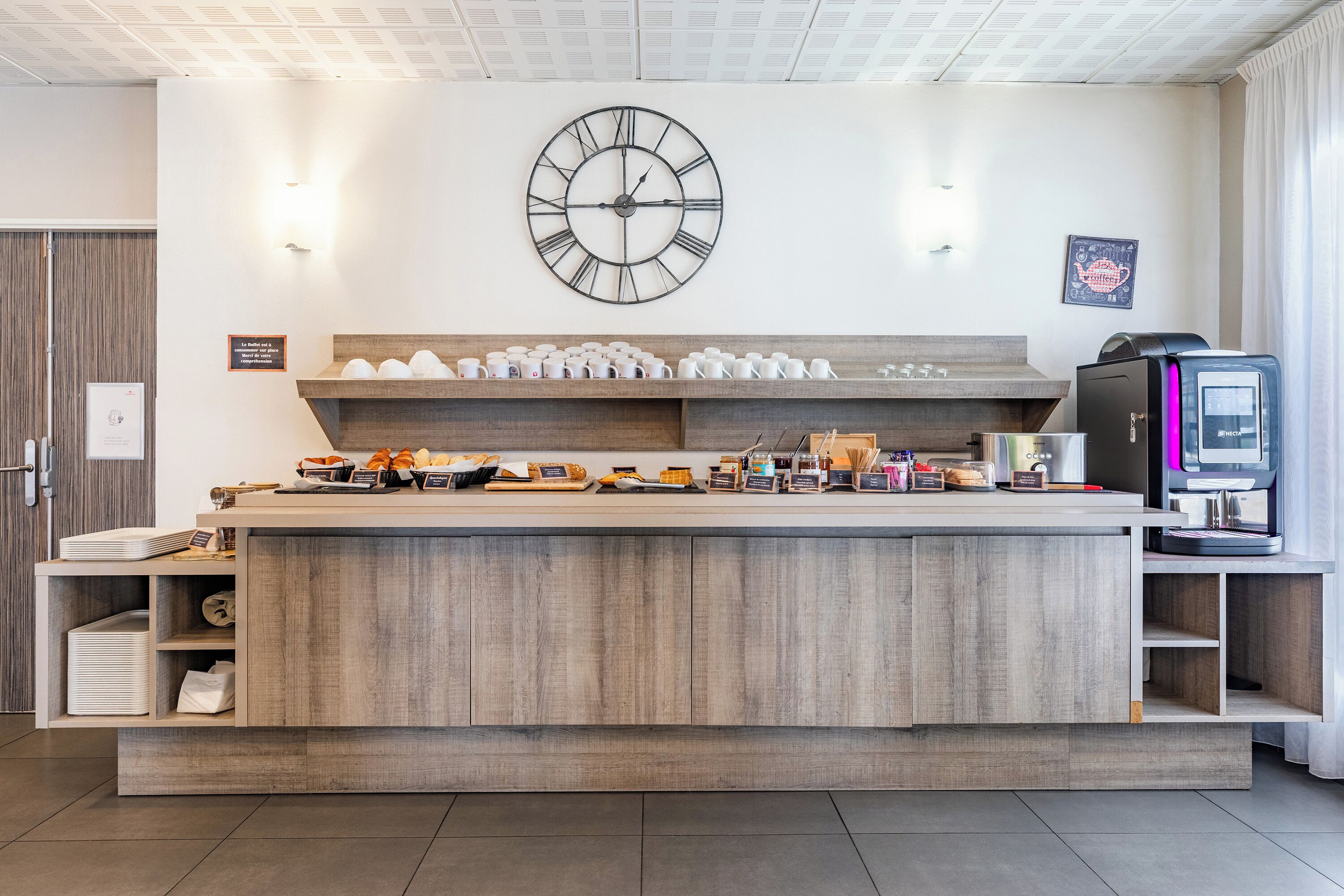 A modern reception area with a wooden counter, a large wall clock, and a coffee machine.