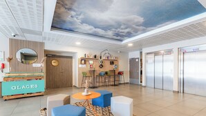 A modern lobby with a cloud-themed ceiling, a reception desk labeled 'GLACES', and a seating area with blue and white furniture.