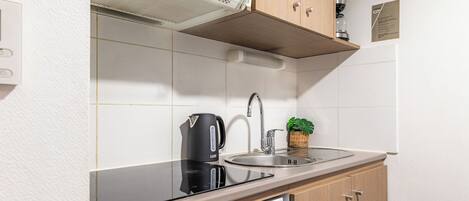Uma cozinha moderna com fogão por indução preto, pia de aço inoxidável e armários de madeira.