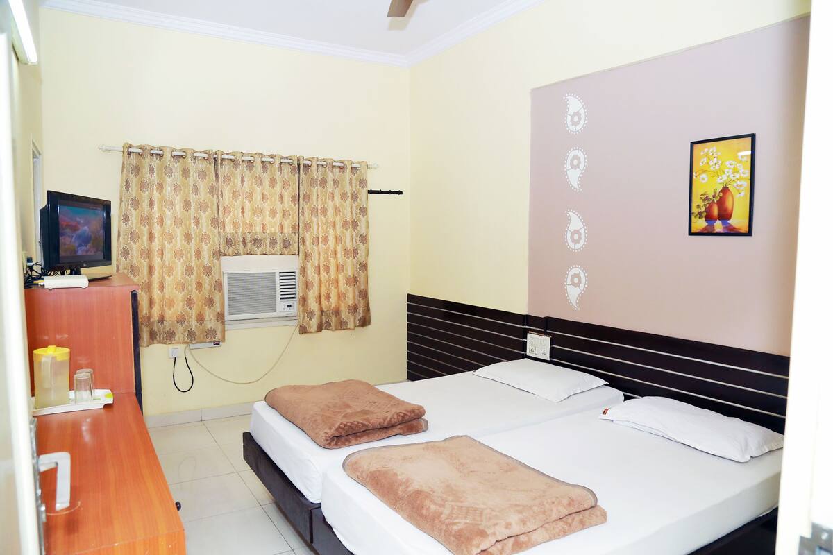 Quarto de hotel com cama, escrivaninha, televisão, ar condicionado e janela com cortinas.