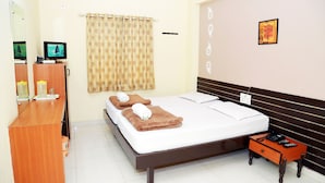 A hotel room with a bed, a small wooden side table, a television, and a bathroom area. - Hotel Geetanjali (Hyderabad)