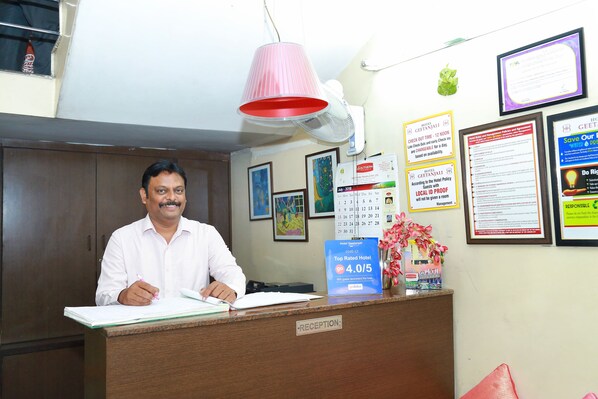 Un mostrador de recepción de hotel con un hombre escribiendo, un calendario y varios carteles informativos en la pared.