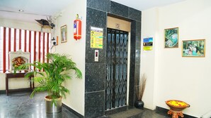 A lobby with a reception desk, a potted plant, a fire extinguisher, a door with a security keypad, and two framed artworks. - Hotel Geetanjali (Hyderabad)