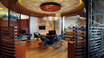 A modern interior with a wooden reception desk, blue chairs, a round table, and a unique ceiling design.